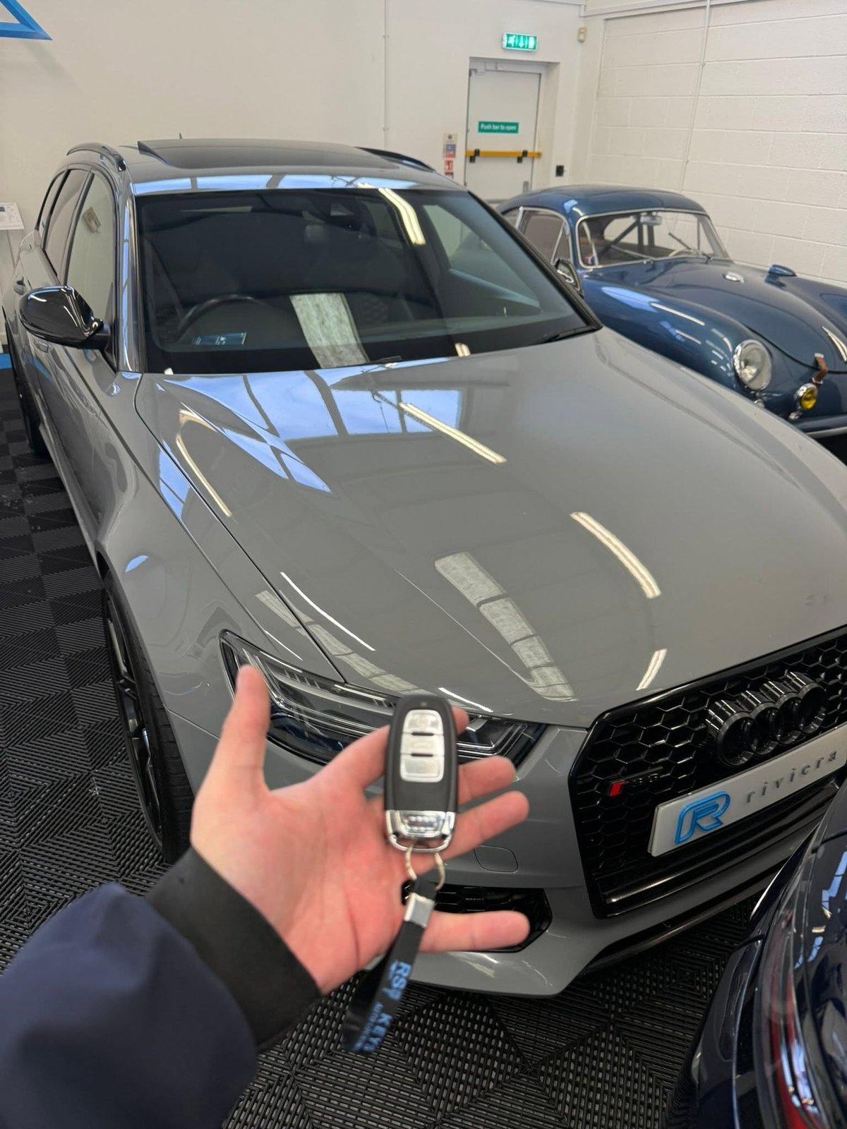 Person holding car key in front of gray SUV in indoor garage showroom — RS Keys vehicle attended in Ryde