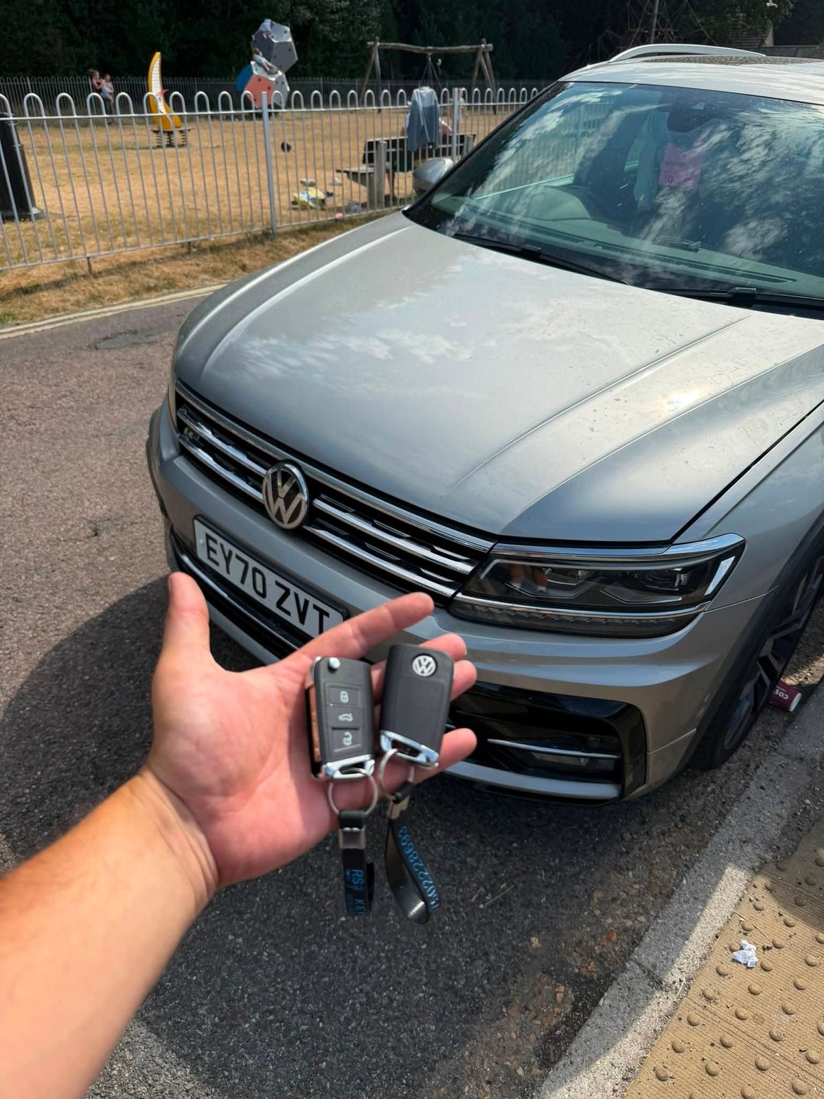 Hand holding Volkswagen car key fob in front of silver VW vehicle parked on driveway
