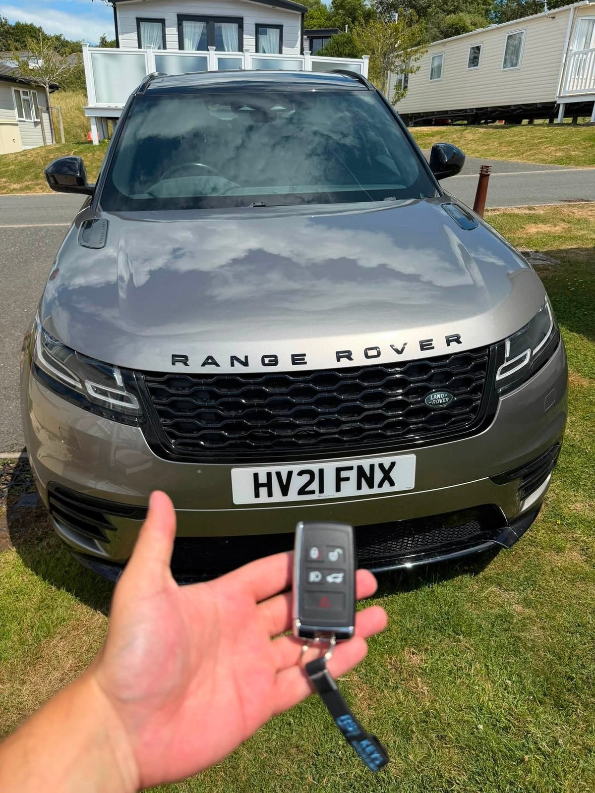 Person holding a Range Rover key fob in front of a silver Range Rover SUV parked in a residential area