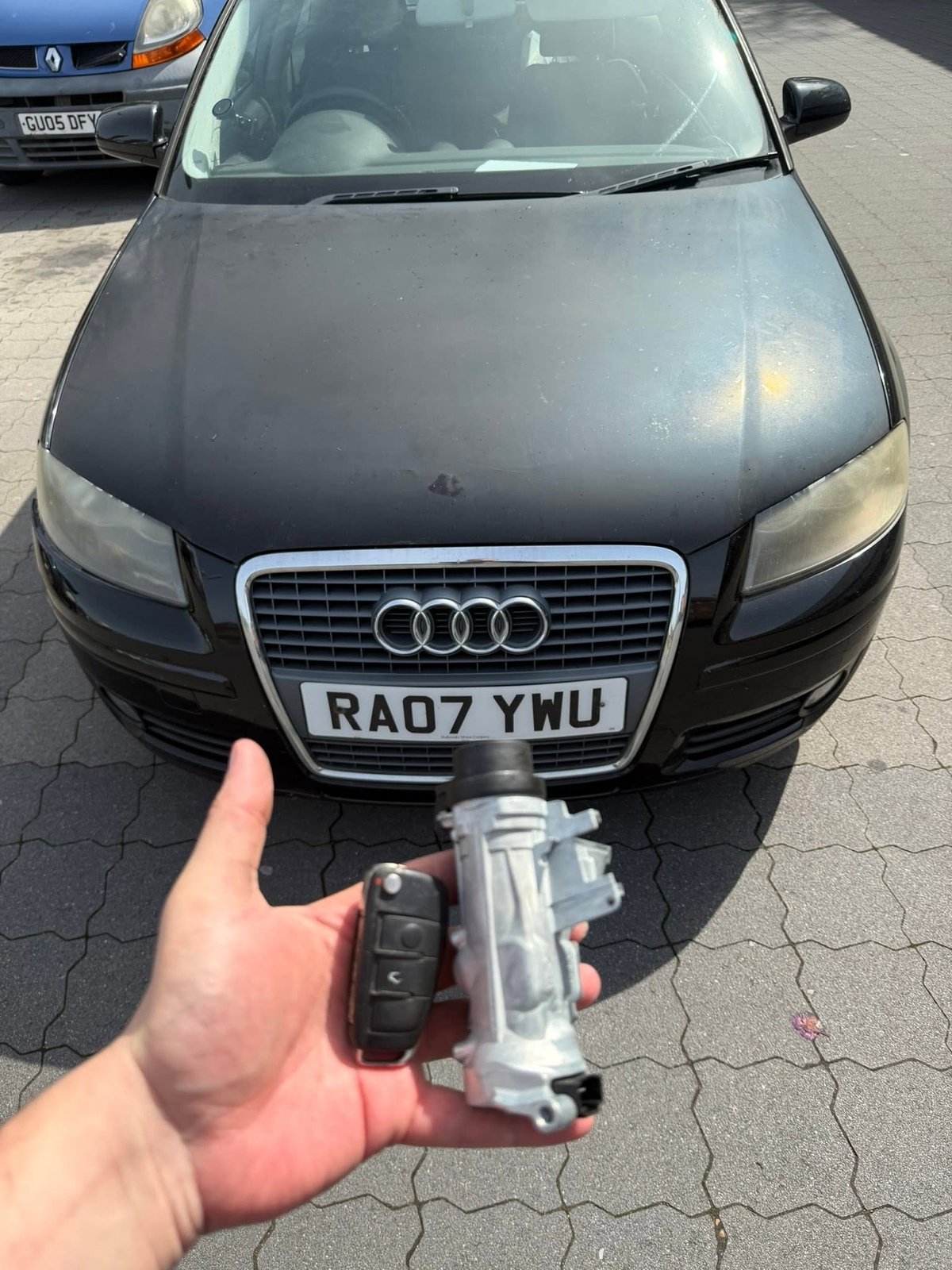 Person holding an Audi car key fob in front of a black Audi sedan
