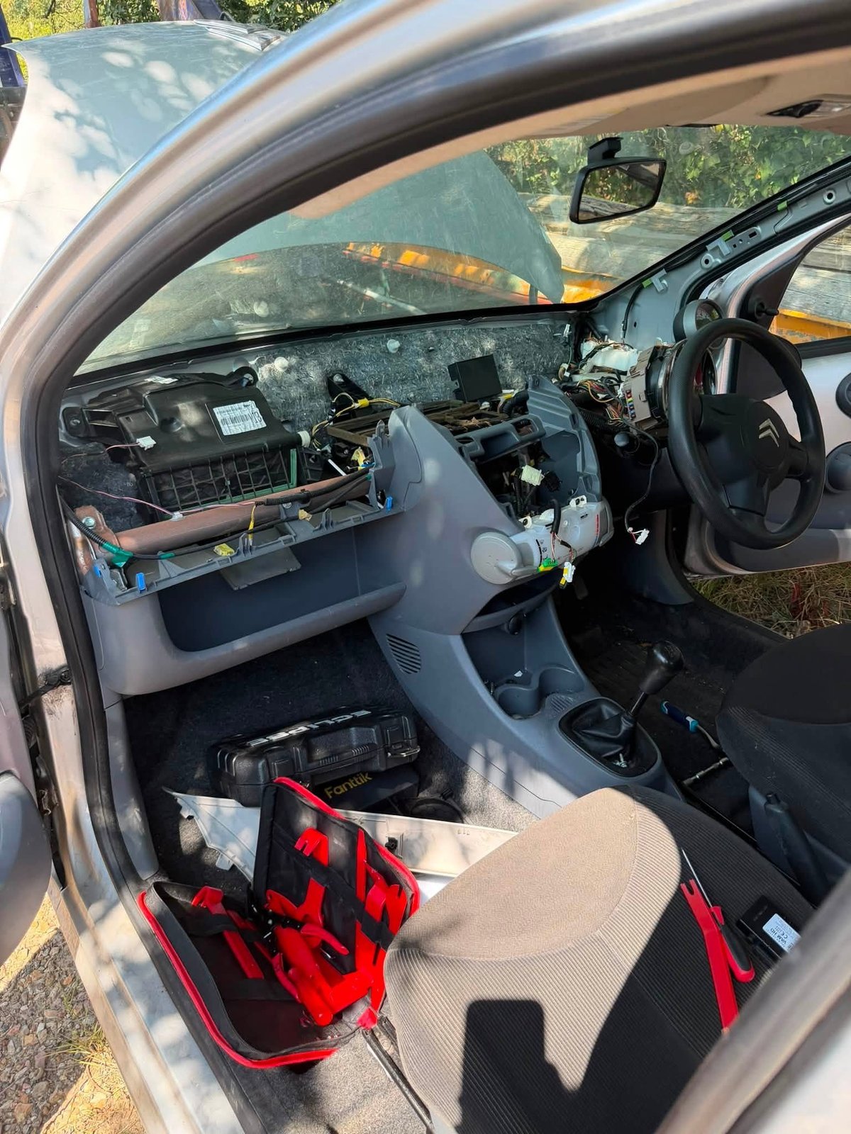 Interior of a disassembled car showing the steering wheel, dashboard, and exposed wiring with red and black components visible on the seats